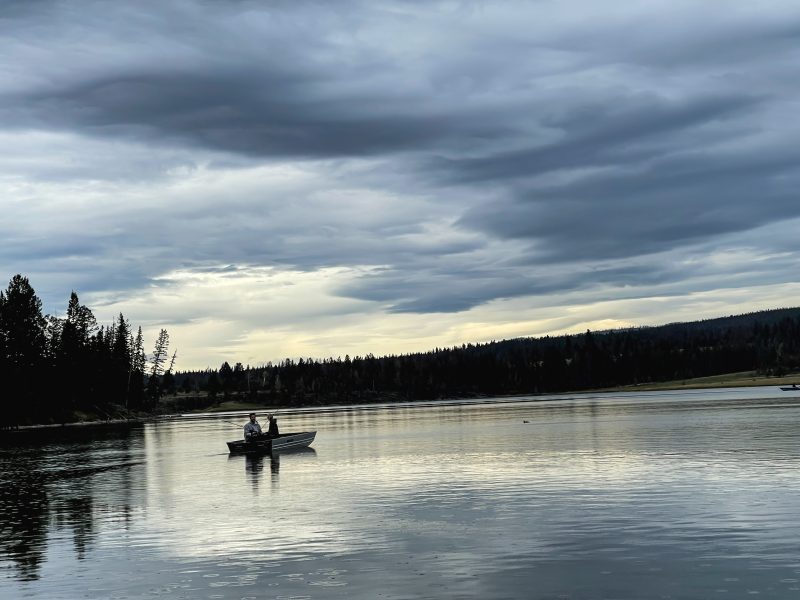 Two anglers fishing from a small aluminum boat on calm water under a moody grey sky at Leighton Lake