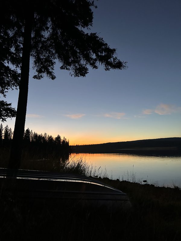 Canoe resting on the shore of Leighton Lake at dusk with an orange sunset reflected in the still water