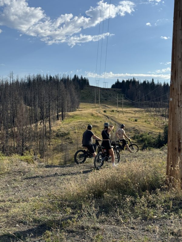 Three riders pausing on a grassy trail beneath powerlines near Leighton Lake