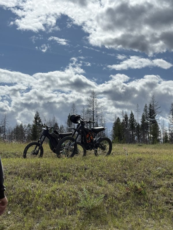 Two electric trail bikes parked in a grassy meadow under a dramatic cloudy sky near Leighton Lake