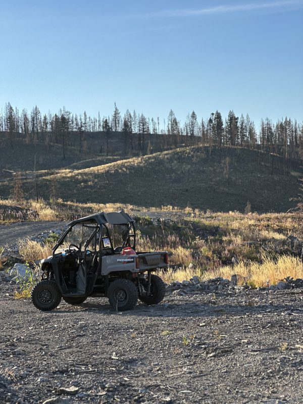 Side-by-side off-road vehicle parked on a gravel road with fire-scarred hills behind, near Leighton Lake