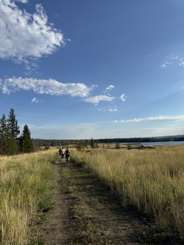 Two cyclists riding a grassy lakeside trail at Leighton Lake with rolling hills in the distance